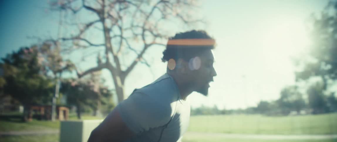 Man in gray shirt warms up outdoors in sunny park with blooming trees in the background