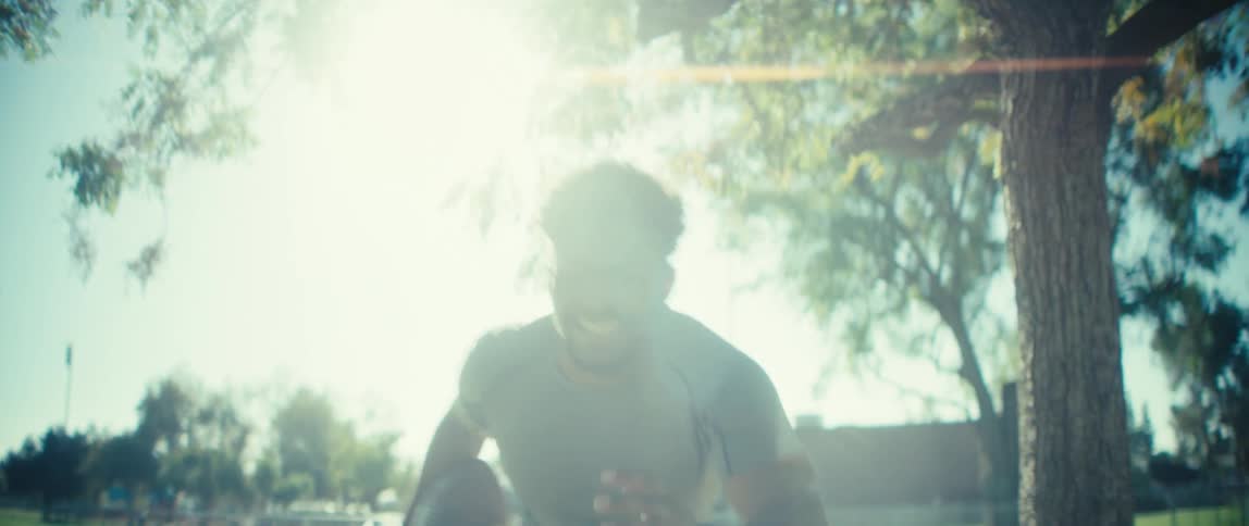 Man in gray shirt and light shorts runs along paved path in green area with trees and fences in the background