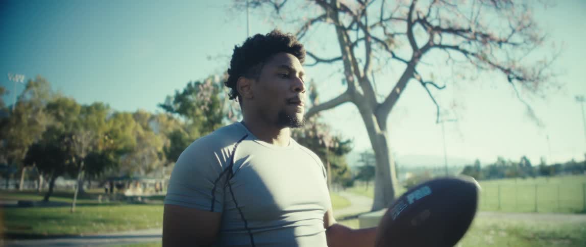 The video is an extreme closeup of a mans face heavily squinting and focused on a task with an expression of intense concentration or minor strugglehe is wearing a grey athletic shirt and appears to be outdoors in a sunny park setting breat