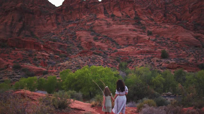 A woman and a child hold hands while walking across a rough rocky formation at midday