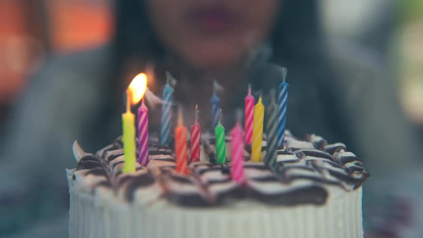 A woman sits behind a birthday cake and blows out the candle after making her wish