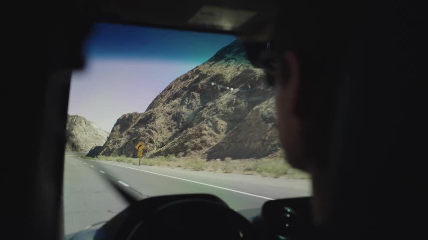 Man driving a car on a road next to a rocky hill indoors during day time