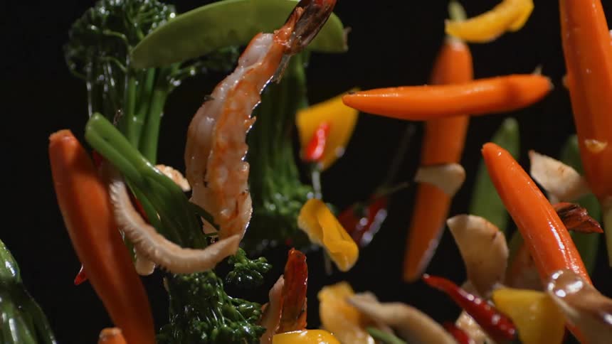 Vegetables and seafood are tossed in a pan