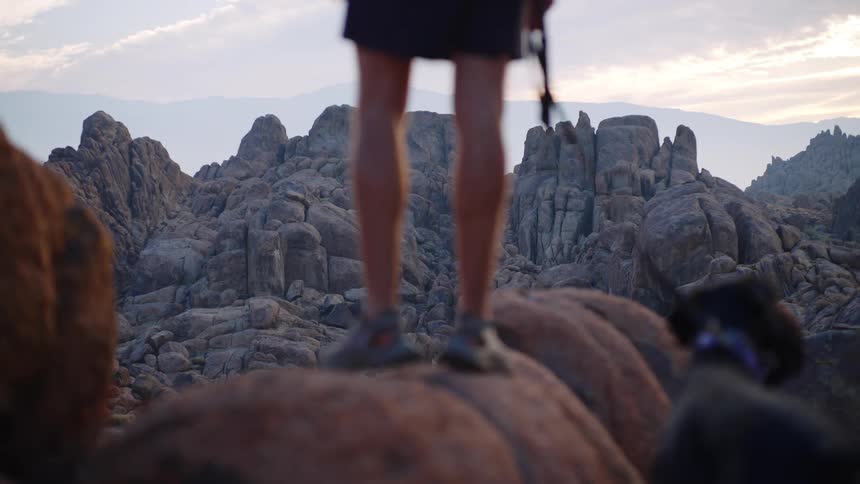 A man straps a rope onto his dog while standing on a rocky cliff during a midday hike