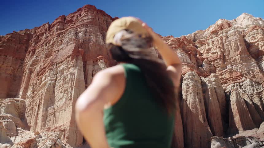 A female explorer wearing a hat gazes at a tall mountain beside her on a sunny day