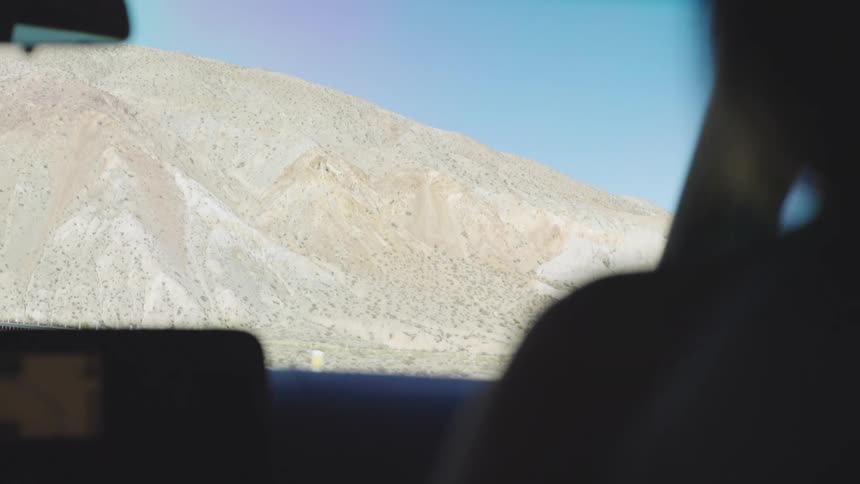 Silhouette of person inside vehicle looking out at desert landscape with blue sky and rocky hills
