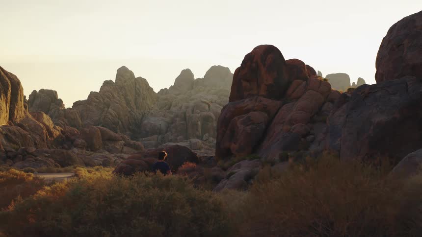 A lone hiker walks with a dog through a rocky desert canyon at sunset