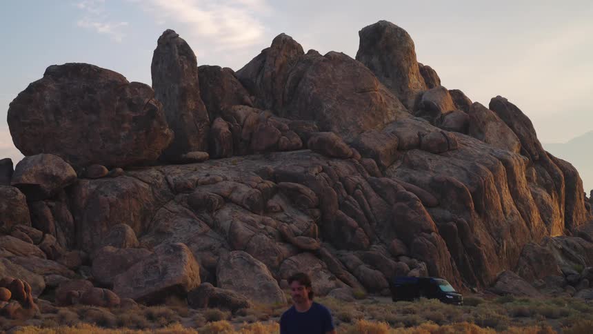 A man walks near a camping van by massive rocky formations at sunset