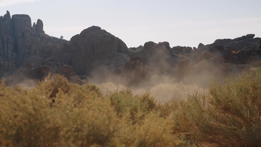 A van drives on a dirt road kicking up dust in the mountains
