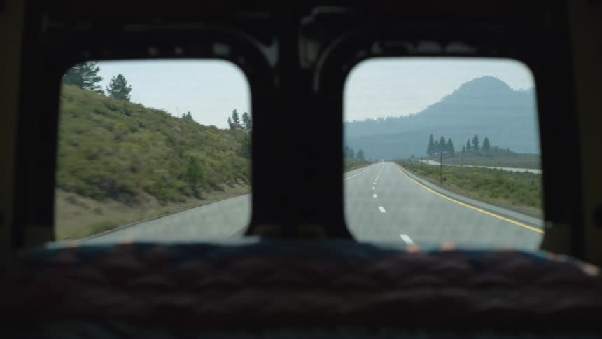 A car drives on a freeway with grass lining both sides of the road at midday