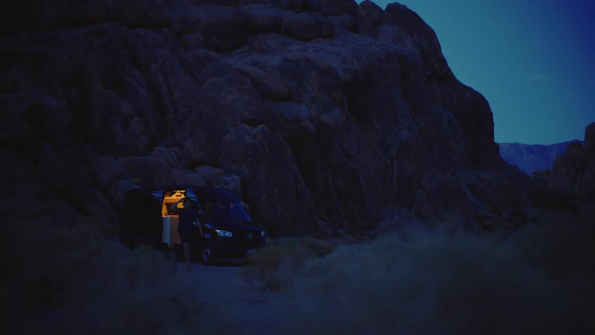 A man walks near a van parked off road near some rocky cliffs