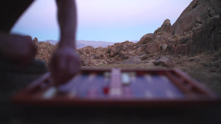 Two people play a board game near rocky canyons at dusk