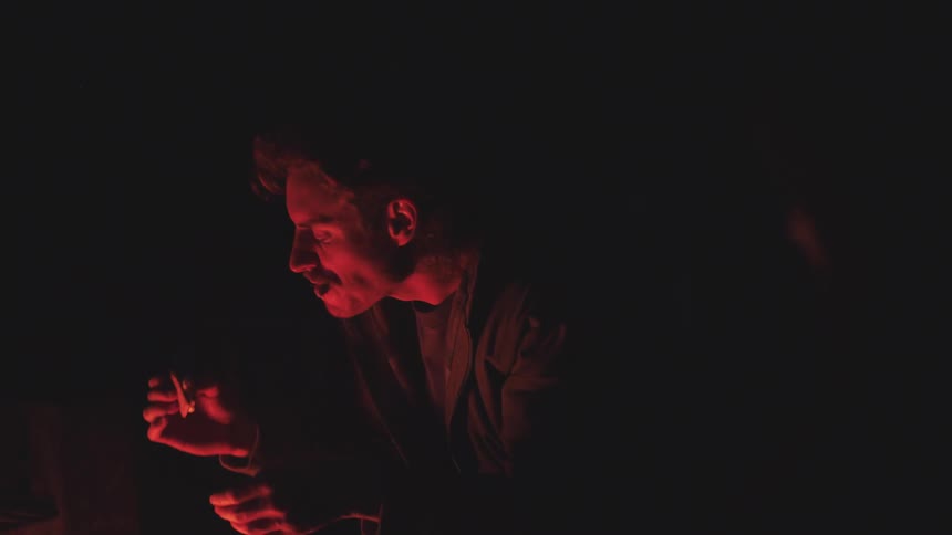 Illuminated by the warm glow of a campfire a man eats a piece of food in the dark