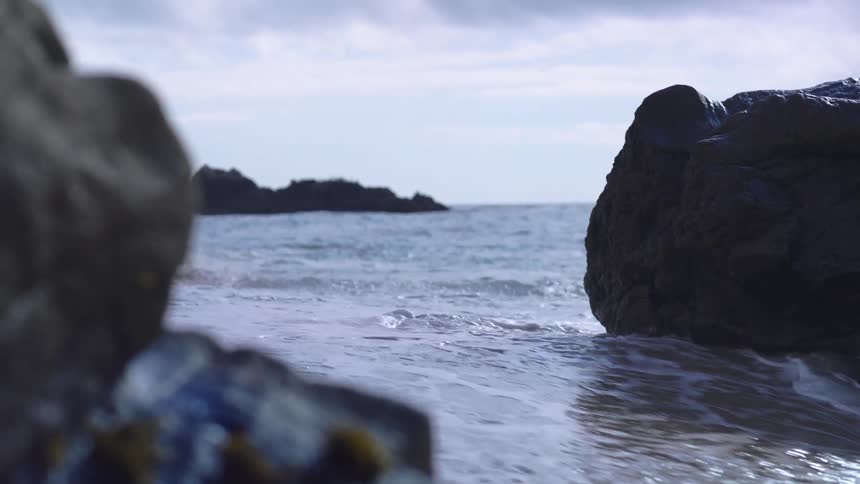 Light sand touched by gentle waves between large rocks and partly cloudy sky