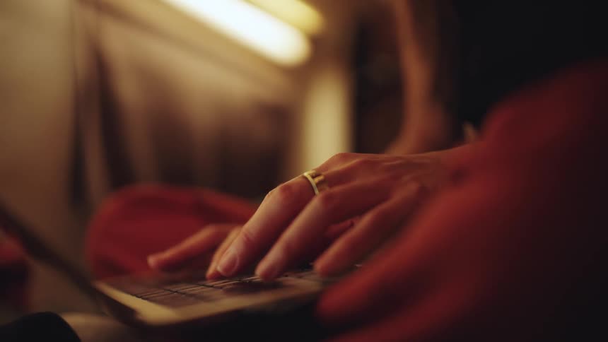 Fingers typing on a laptop keyboard under warm light in a cozy setting
