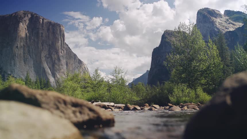 Valley surrounded by mountains and a shallow river under a partly cloudy sky