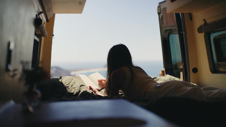 A young woman lying in a motorhome reading a book
