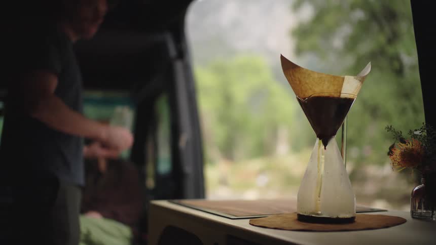 A coffee dripper brews on a van counter as a couple relaxes during van life
