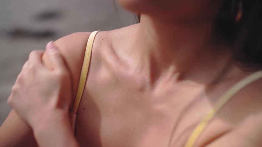 A closeup of a woman applying sunscreen to her shoulder in sunlight
