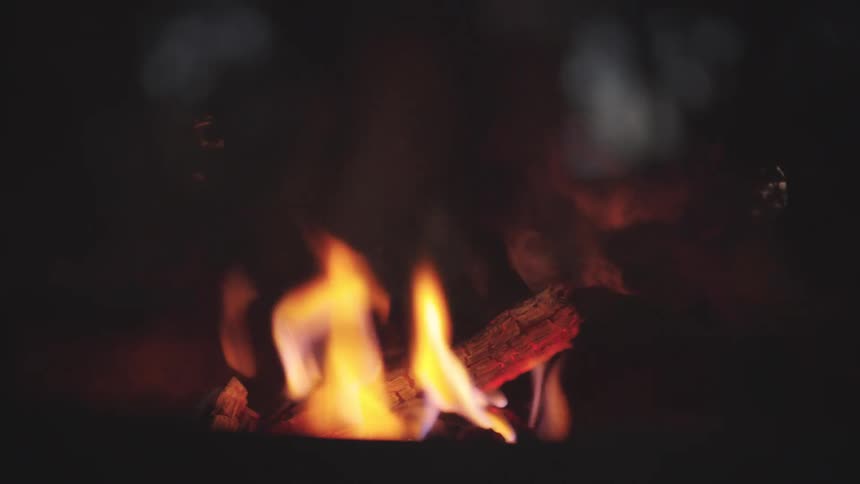 Bonfire burning with the legs of a person standing next to it outdoors during night time