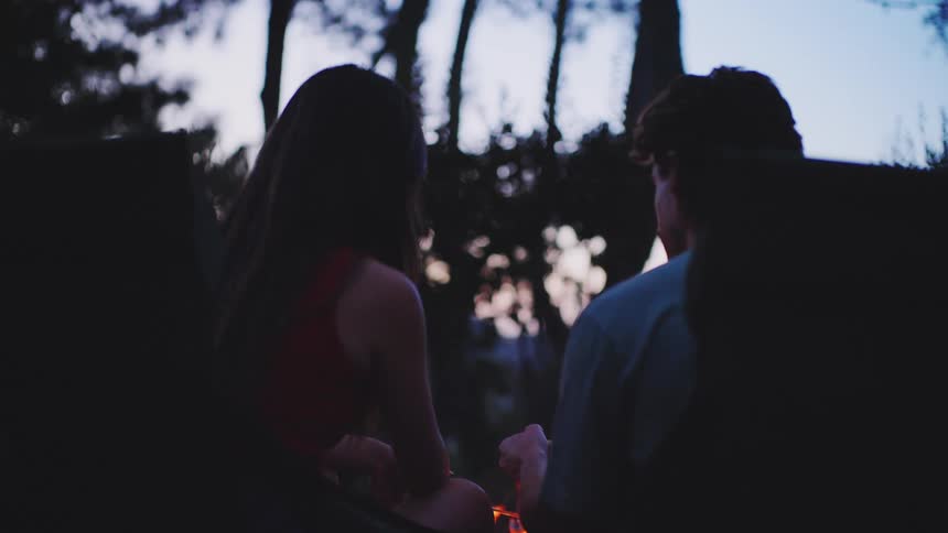 Woman roasting marshmallows over a campfire in the evening gestures after the man she was talking to leaves