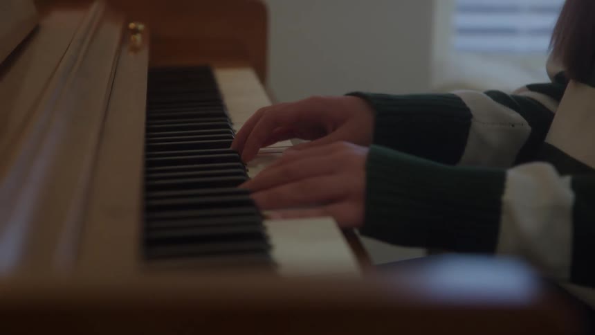Person playing wooden piano with striped shirt and hands on keys in softlit setting