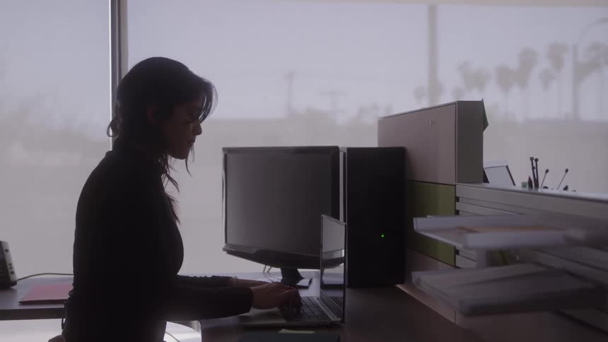 A woman works on her laptop at a desk in a softly lit modern office