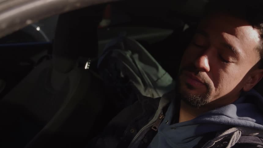 Man covers his face with his hand while sitting inside a car