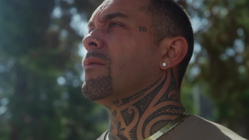 Hispanic man standing up outdoors next to trees during day time