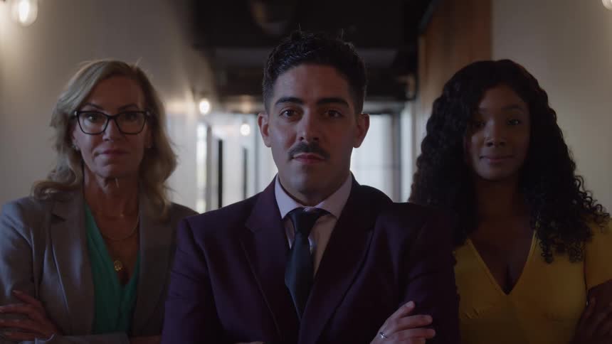 Two women stand beside a man in a hallway with the middleaged woman on the left wearing a suit the woman on the right wearing a yellow dress and the man in the middle wearing a red suit