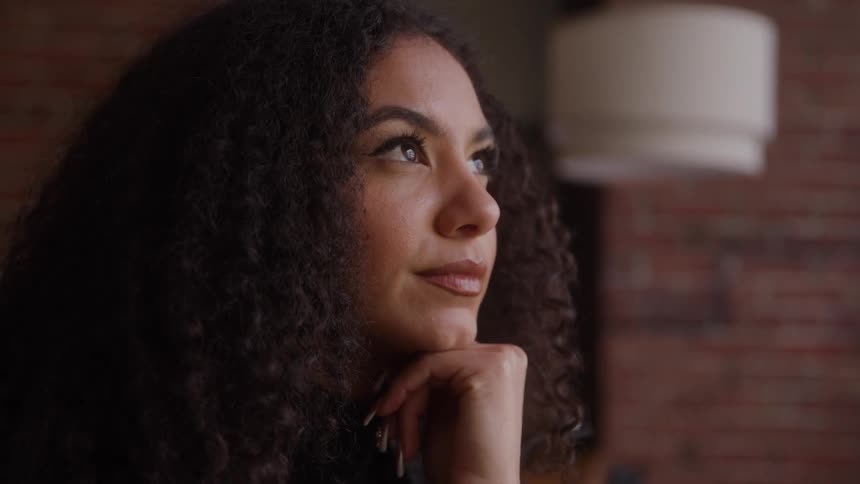 Woman smiles slightly as she leans her chin on her hand while sitting indoors during the day
