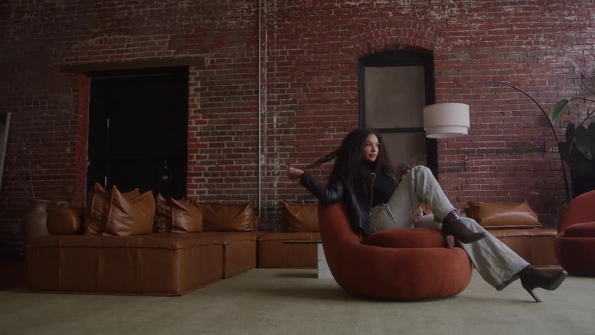 A woman is sitting in a chair with one leg up on the seat and playing with her hair