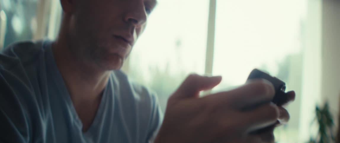 Man in light blue shirt holds phone with both hands in front of sunlit window