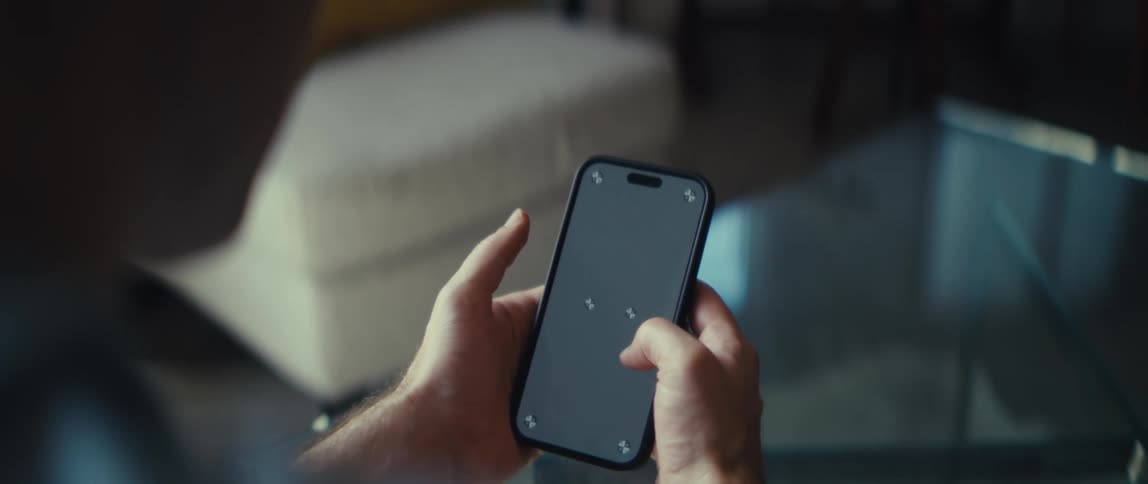 The video is an extreme closeup of a persons hands holding a modern smartphone with a black screen the person is manipulating the screen with their thumbs and there are four small white tracking markers visible in the corners of the phones di