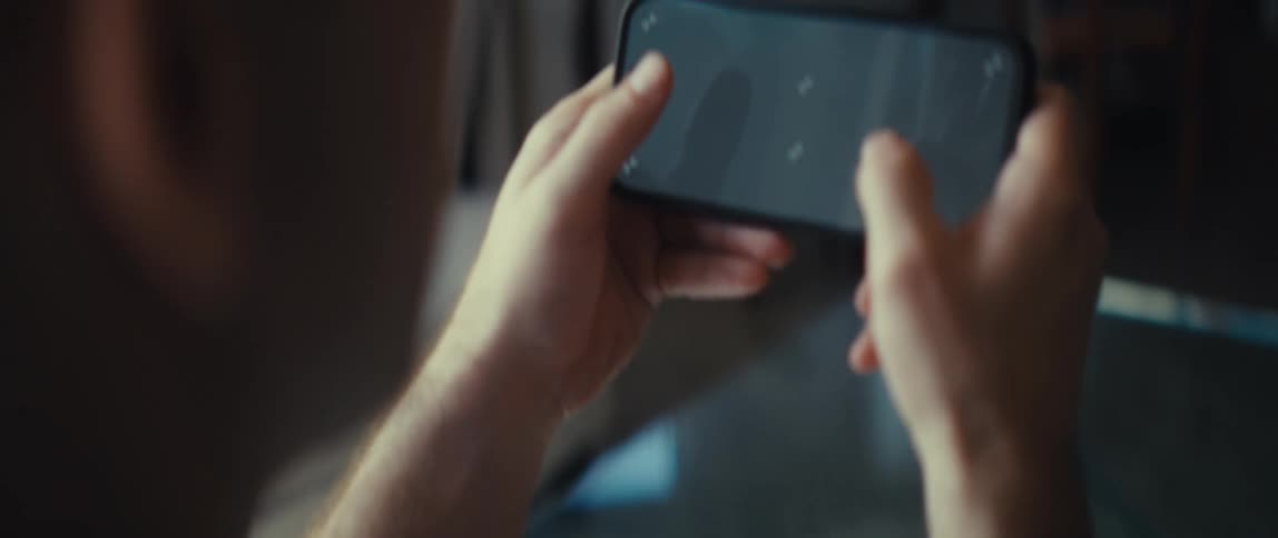 A man sits indoors at midday holding his phone with both hands while using it