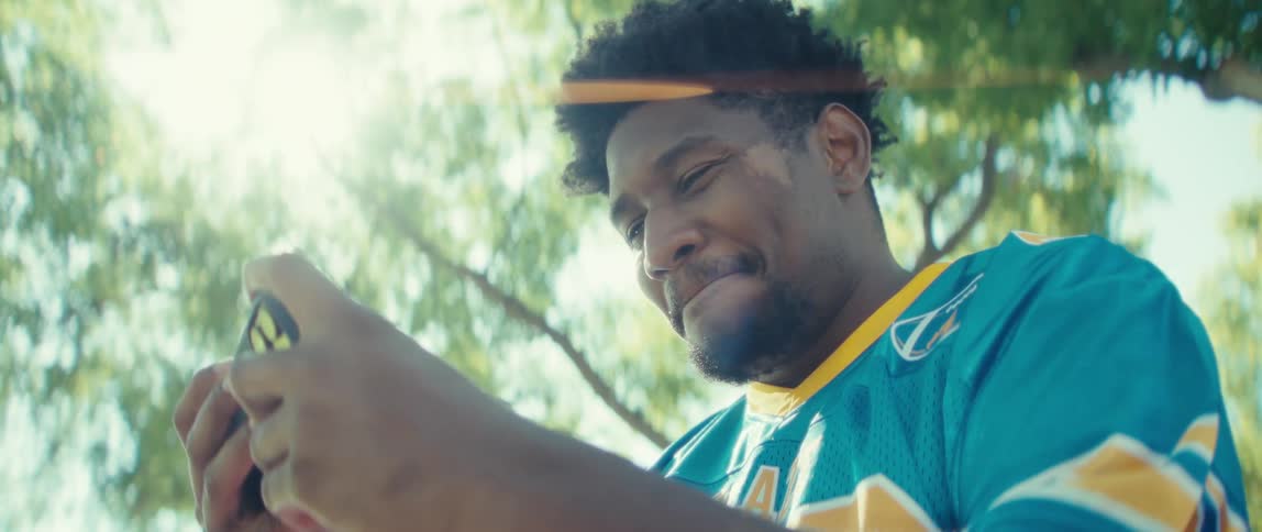 Man smiles while holding his phone under sunlight