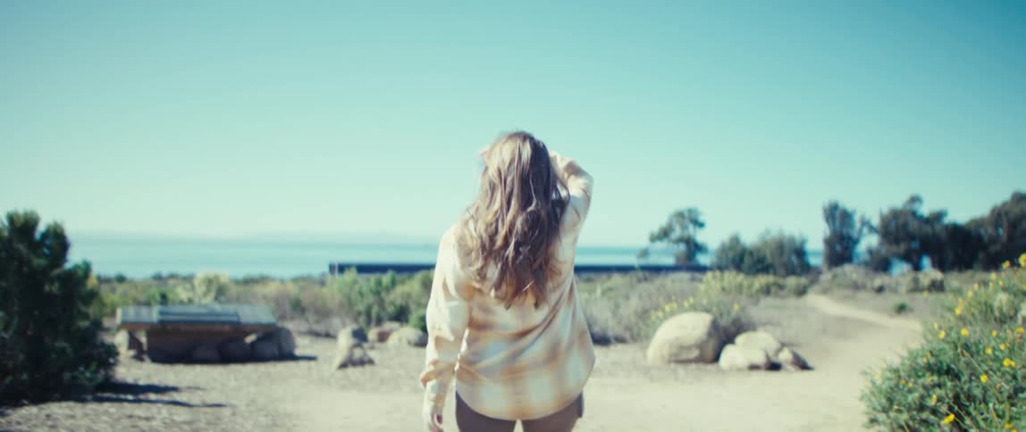Woman walks along a sunny trail toward the sea