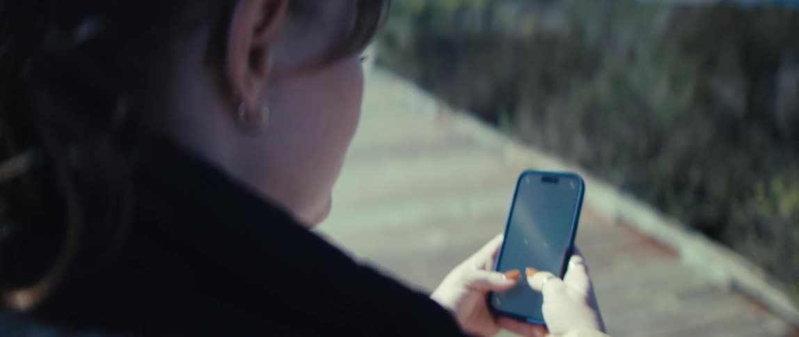 A woman plays a mobile game on her smartphone outdoors in daylight