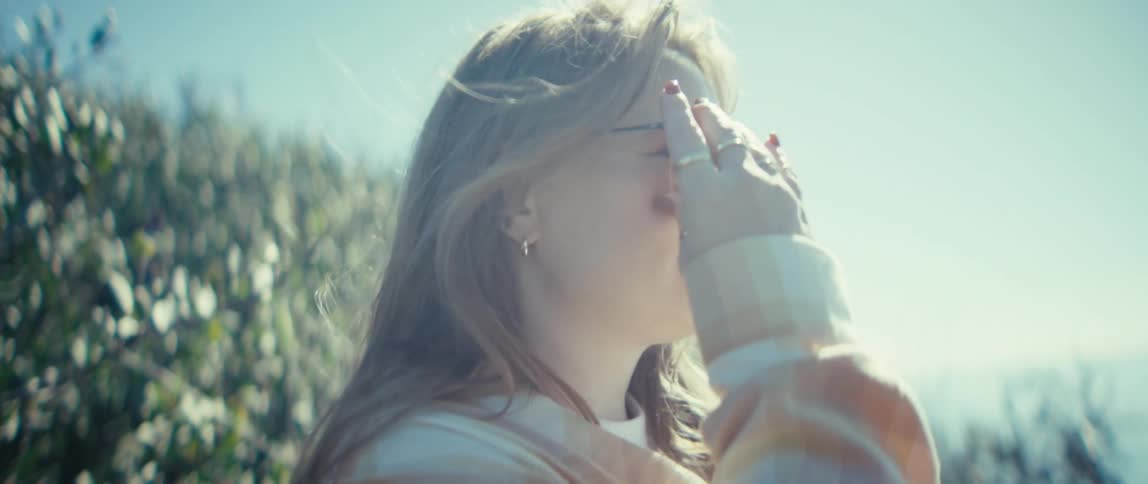The wind blows the womans hair as she puts on her sunglasses