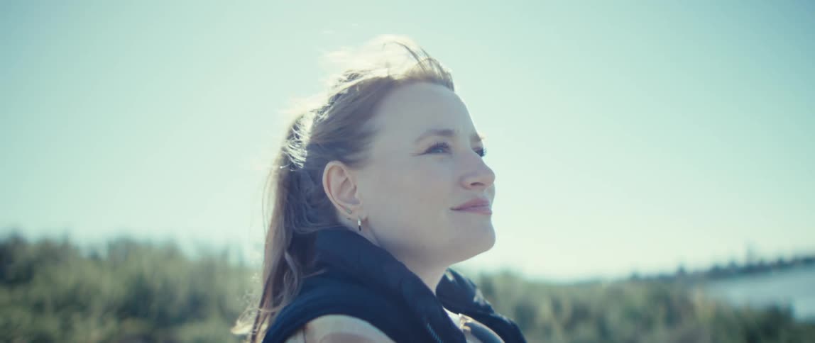 The woman smiles on a windy day by the lake