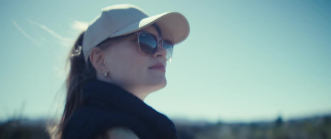 The video is an extreme closeup of a persons face looking up toward the bright sky they are wearing a lightcolored baseball cap and dark sunglasses while outdoors in a sunny arid environment