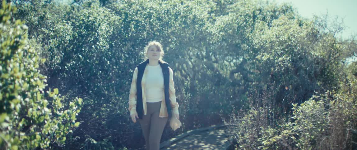 Person walking on a trail surrounded by vegetation under bright sunlight