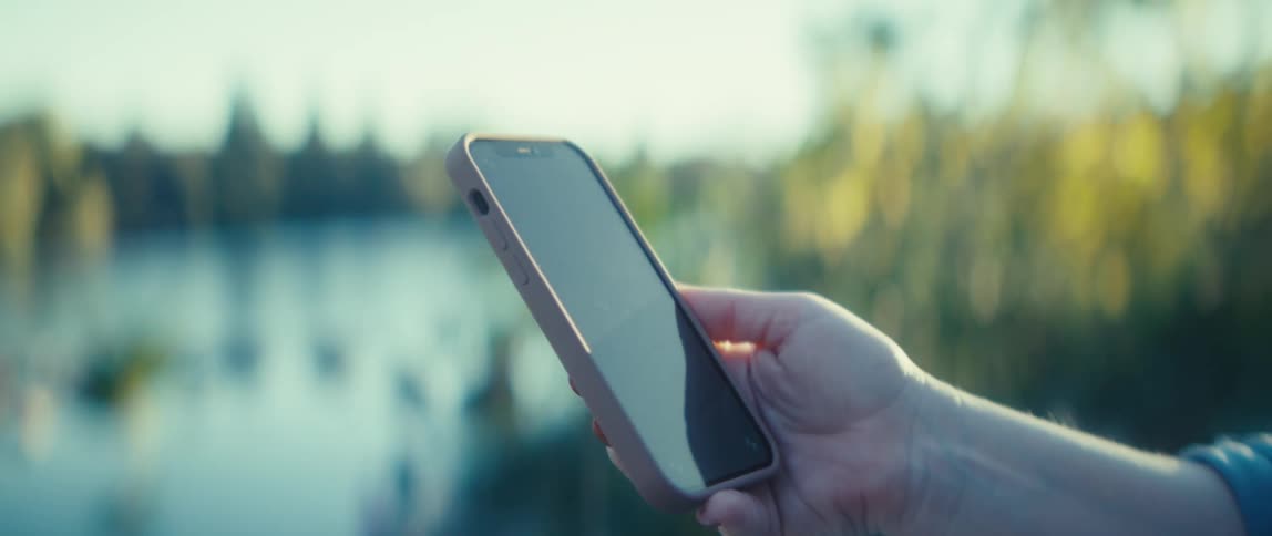 The woman taps her phone by the lake