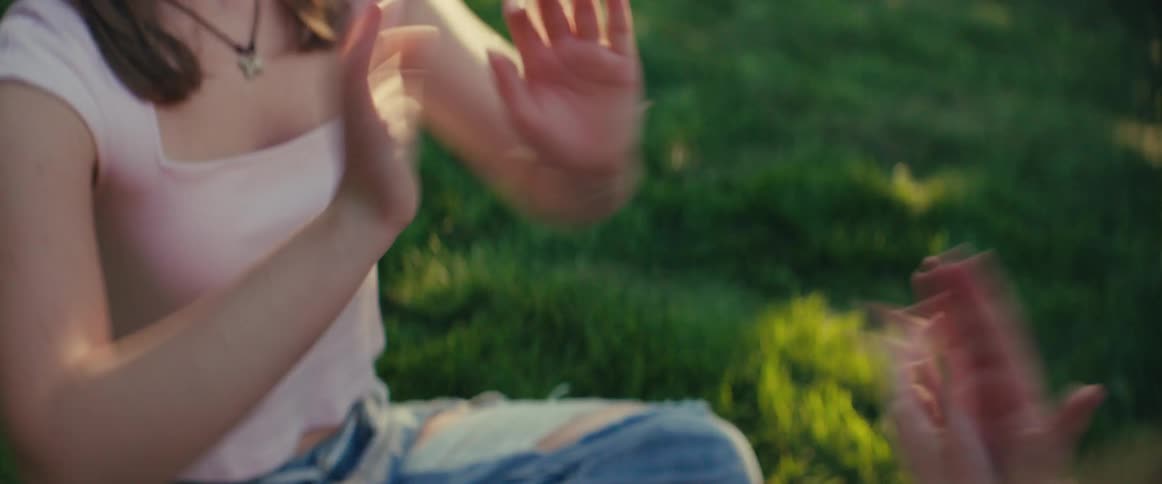 Two people play clapping hands while sitting on the grass