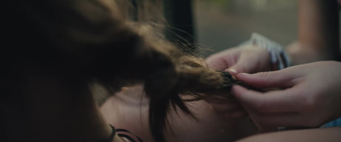 Hands braid strands of hair in an outdoor setting