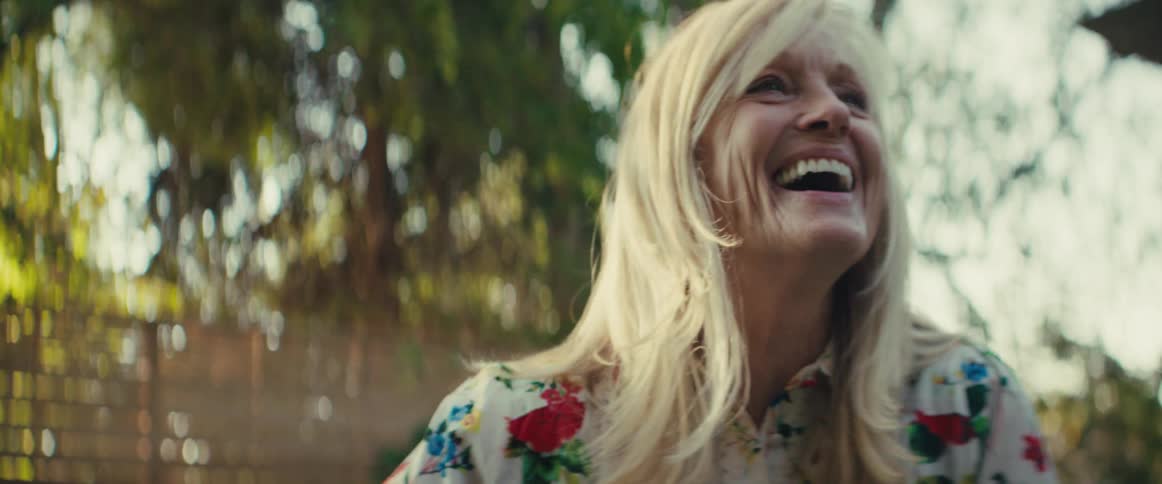 A woman is outside and laughs as she reaches for something