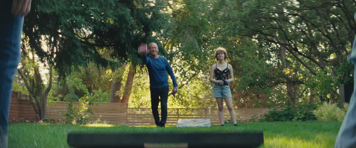 Man throws a bean bag as a young woman watches on a sunny lawn