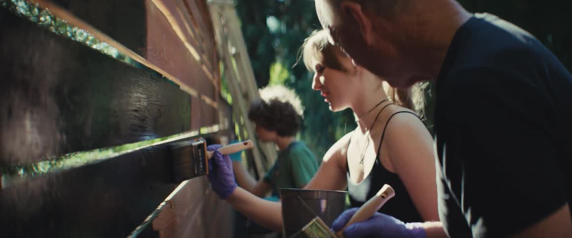 Group paints a wooden fence under sunlight on a clear day