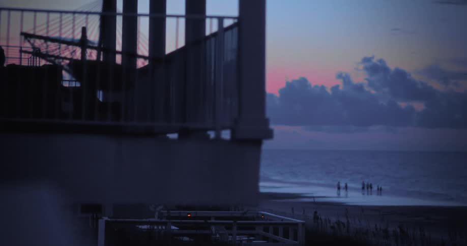 Group of people walking on the beach at dusk seen from a balcony