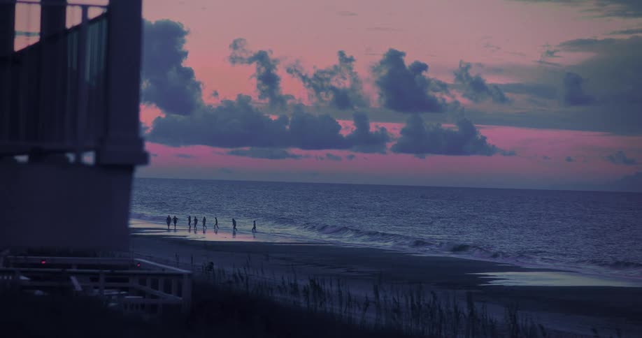 A group of people are on a beach as the sun sets